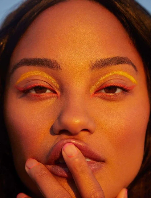 Close-up portrait of an adult woman with yellow and red eyeliner, fair skin, and dark hair, with a finger near her lips.