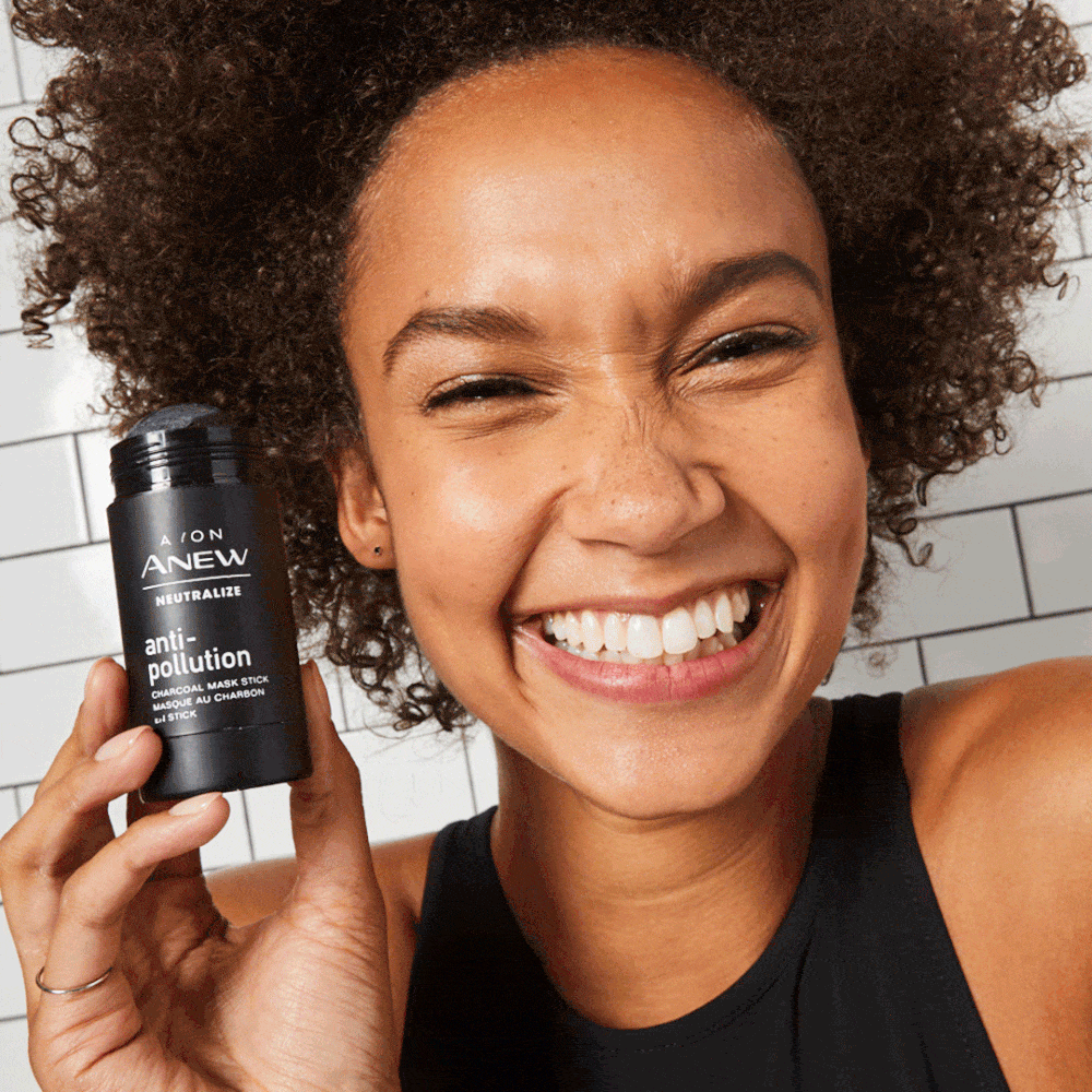 Smiling woman holding a black skincare product stick to promote beauty and skincare, with a tile background and natural lighting.