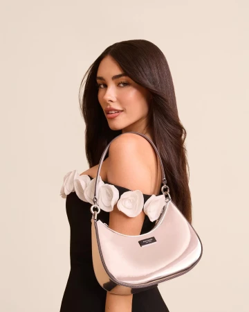 Madison Beer poses with a shiny silver Kate Spade purse in a studio portrait, wearing a black dress with white floral embellishments.
