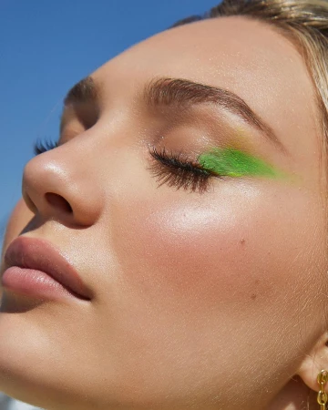 Close-up portrait of a woman with vibrant green eyeshadow and glowing skin under clear blue sky by Tory Rust