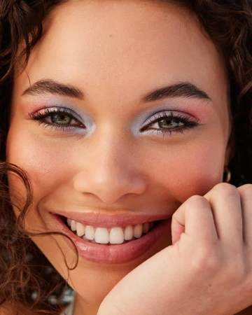Close-up portrait of a smiling young woman with curly hair and colourful eyeshadow photographed by Tory Rust.
