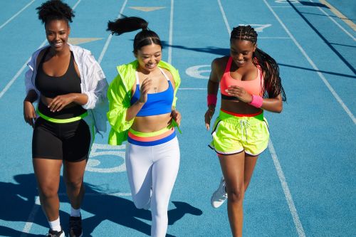 Three adult women are running together outdoors on a blue track wearing sporty clothing in bright sunlight. Fitness and teamwork.