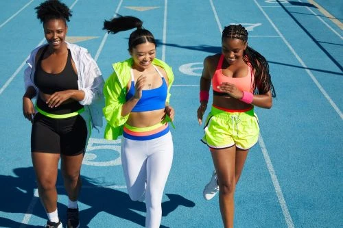 Three adult women are running together outdoors on a blue track wearing sporty clothing in bright sunlight. Fitness and teamwork.