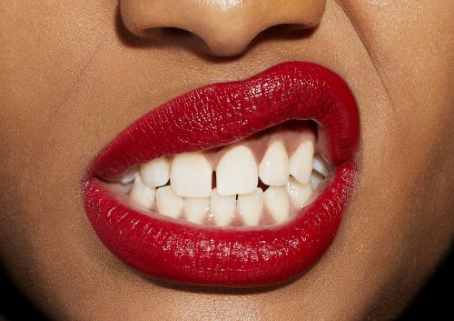 Close-up of lips wearing vibrant red lipstick with teeth biting the lower lip, captured by photographer Tory Rust.