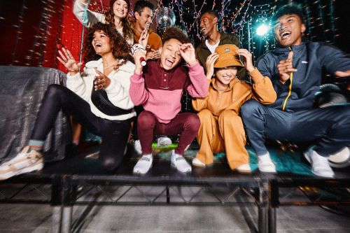 Group of young adults in casual fashion apparel poses on a stage under disco lights with dynamic energy and joyful expressions, capturing a vibrant, candid moment.