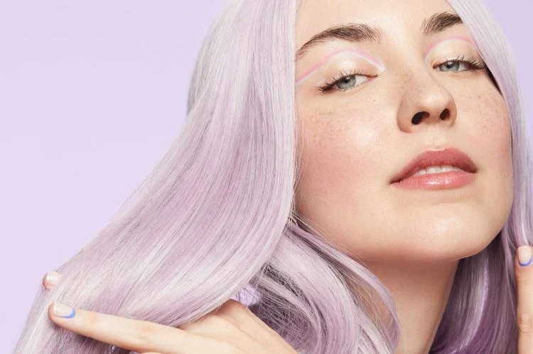 Close-up of a woman with lilac-colored hair, light pink eye makeup, and a light purple background, showcasing beauty and fashion.