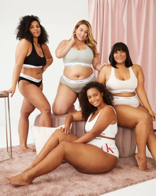 Group of four plus-size women posing in underwear. They wear Calvin Klein branded underwear with a white studio background and soft lighting.