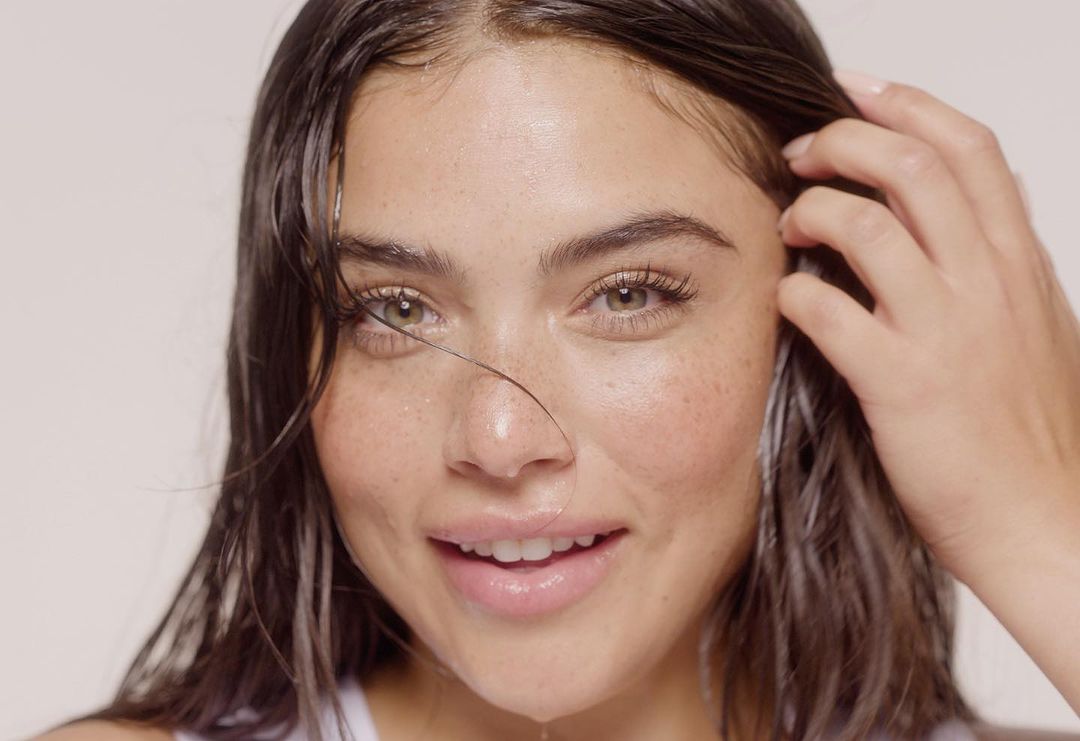 Close-up portrait of a woman with wet dark hair and freckles running her hand through her hair by Tory Rust