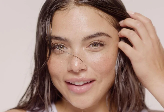 Close-up portrait of a woman with wet dark hair and freckles running her hand through her hair by Tory Rust