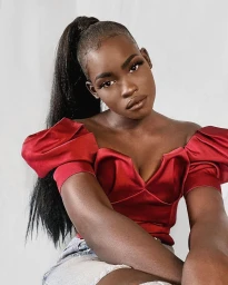 Close-up portrait of a Black woman in a red off-the-shoulder top with a high ponytail against a neutral background.