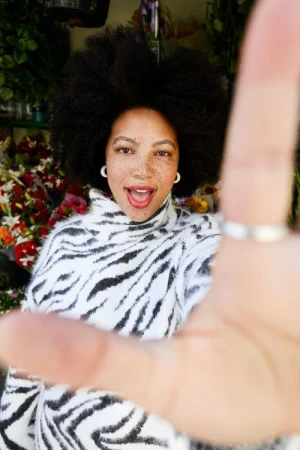 Black woman with afro and freckles wearing zebra print sweater reaching toward camera