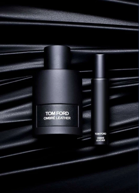 Tom Ford Ombre Leather fragrance still life. A bottle and travel spray are staged on a black satin textile. Perfume and luxury aesthetic.