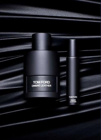 Tom Ford Ombre Leather fragrance still life. A bottle and travel spray are staged on a black satin textile. Perfume and luxury aesthetic.