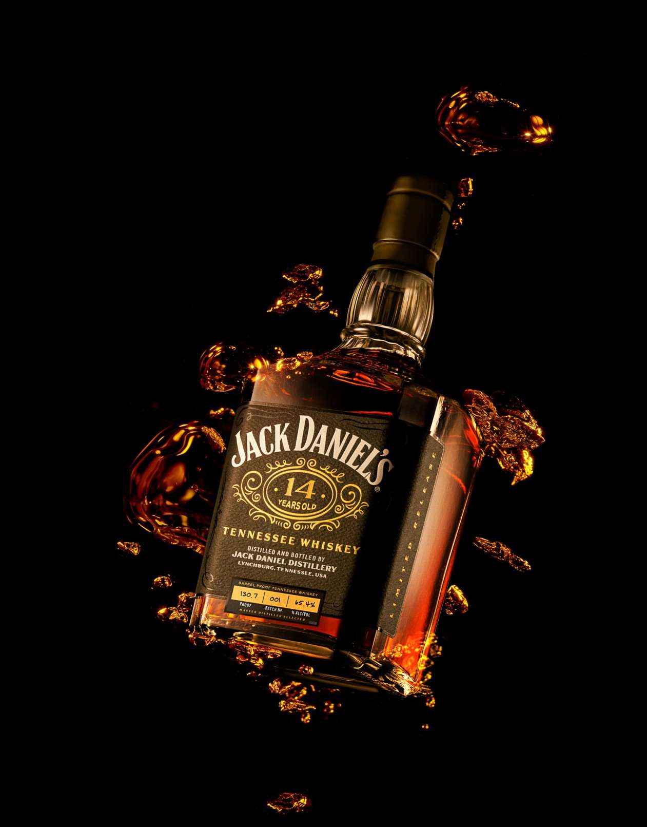 Studio shot of a Jack Daniel's 14 Years Old Tennessee Whiskey bottle, surrounded by whiskey splashes against a black background.