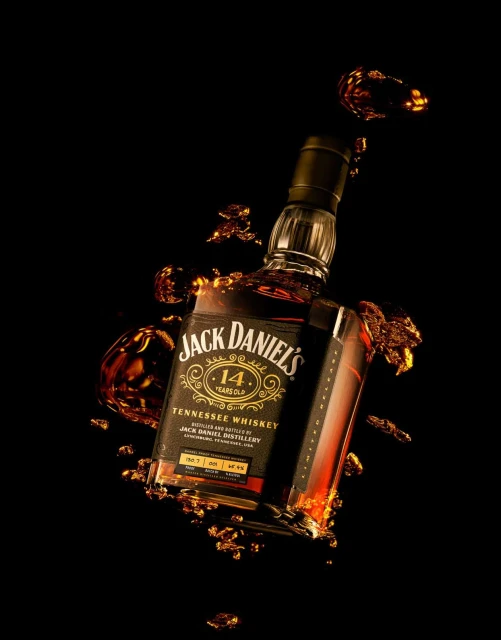 Studio shot of a Jack Daniel's 14 Years Old Tennessee Whiskey bottle, surrounded by whiskey splashes against a black background.