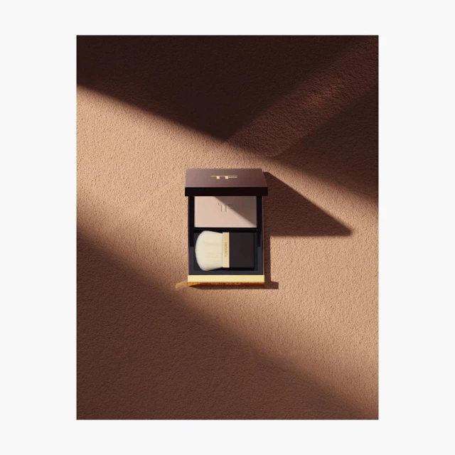 Tom Ford eyeshadow compact with brush. Beauty product shot on a tan background with a shadow overlay.