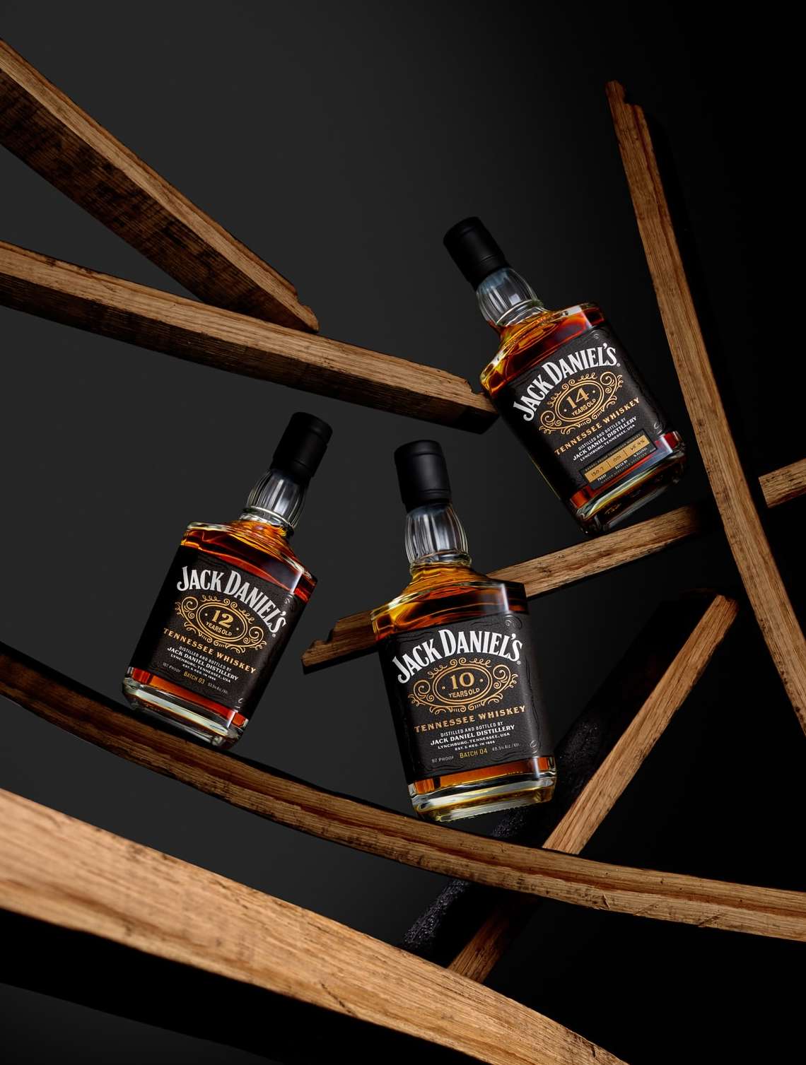 Three bottles of Jack Daniel's Tennessee Whiskey in a studio composition with wooden staves on a dark backdrop. Product photography.