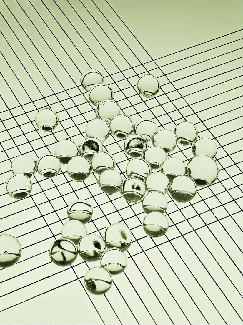 Abstract image of clear glass marbles scattered across a pale green surface with fine black diagonal grid lines, creating an optical effect.