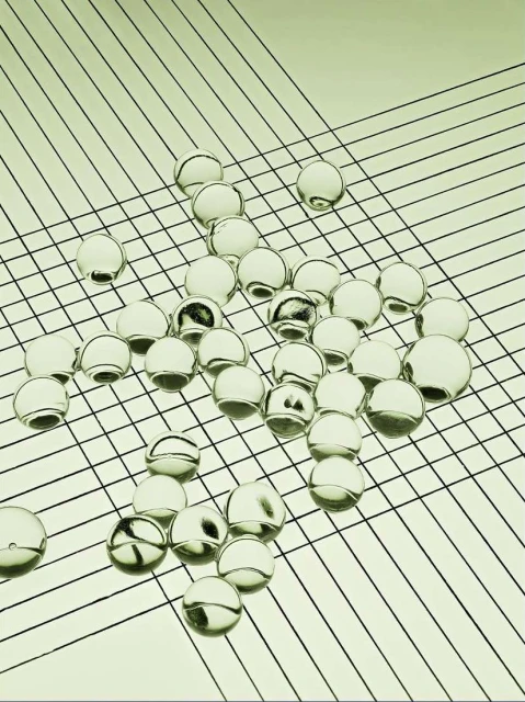 Abstract image of clear glass marbles scattered across a pale green surface with fine black diagonal grid lines, creating an optical effect.