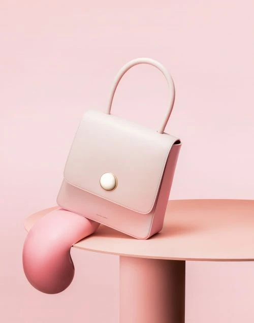 Stylish pink handbag sits on a matching pink table against a pink backdrop, creating a monochromatic, eye-catching fashion product shot.