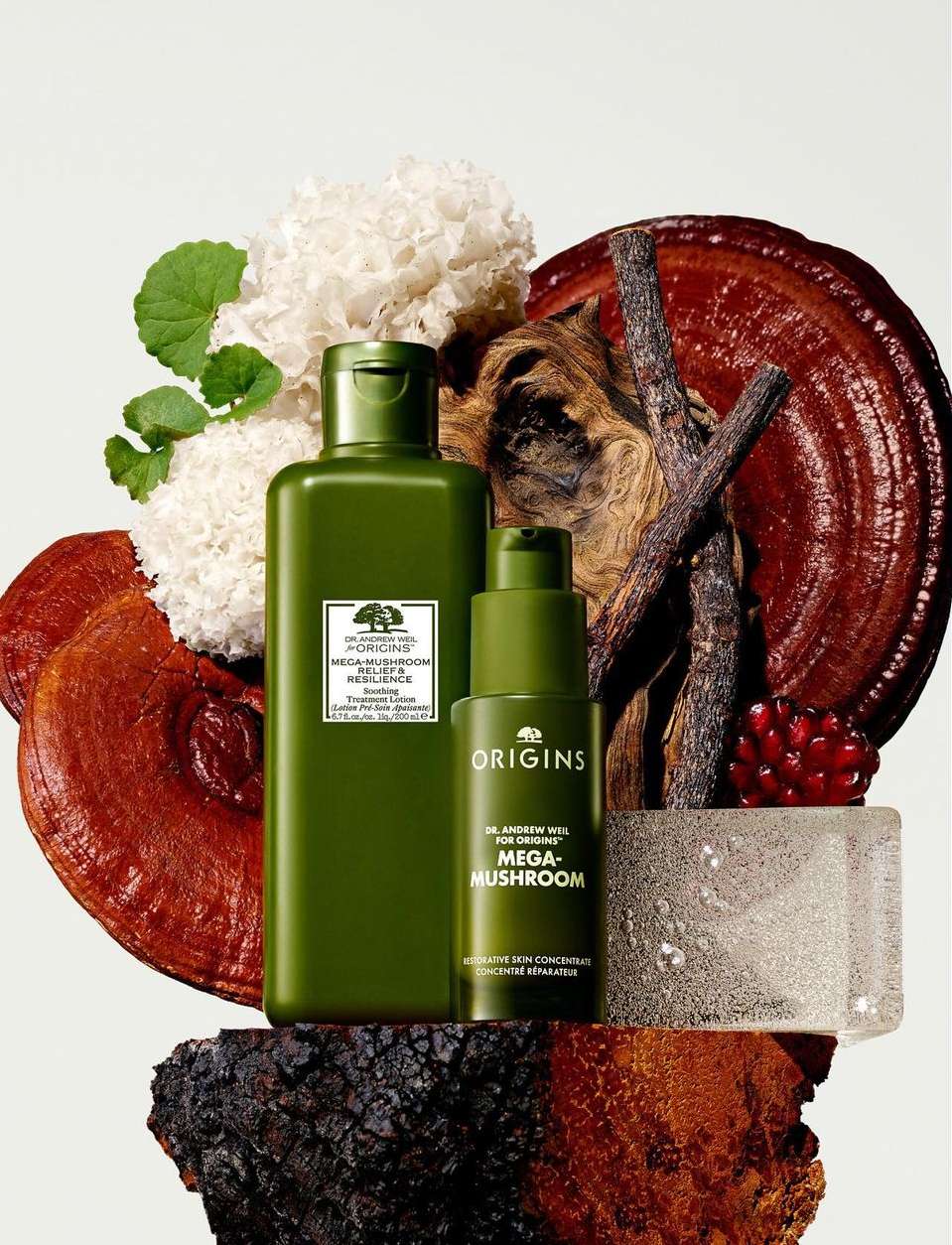Still life shot of Origins skincare products, including face wash and serum, with ingredients like mushrooms against a plain background.