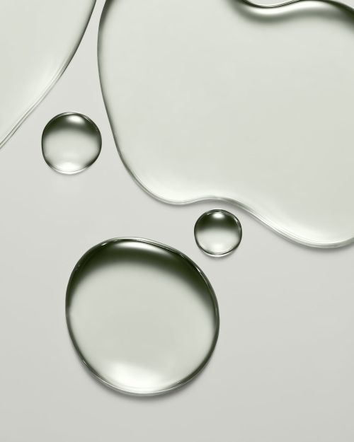Close-up studio shot of clear, round gel droplets and liquid on a light grey surface, showcasing beauty and skincare product texture.