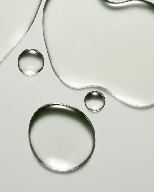 Close-up studio shot of clear, round gel droplets and liquid on a light grey surface, showcasing beauty and skincare product texture.