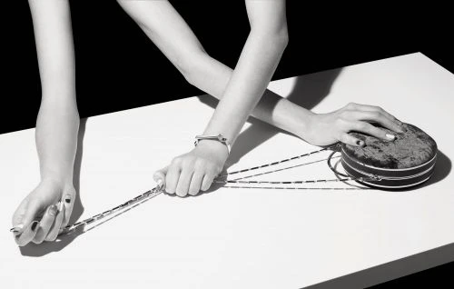 Monochrome shot of a round clutch with chain handle, resting on a white surface, held by an adult woman's hands with painted nails.