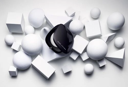 High-angle shot of a black Marc Jacobs compact surrounded by white geometric shapes, including spheres, cubes, and triangles on a white surface.