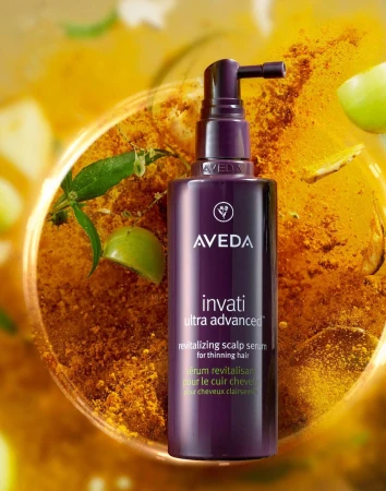 Purple Aveda Invati Ultra Advanced revitalizing scalp serum for thinning hair, showcased on a turmeric powder surface with lime accents.
