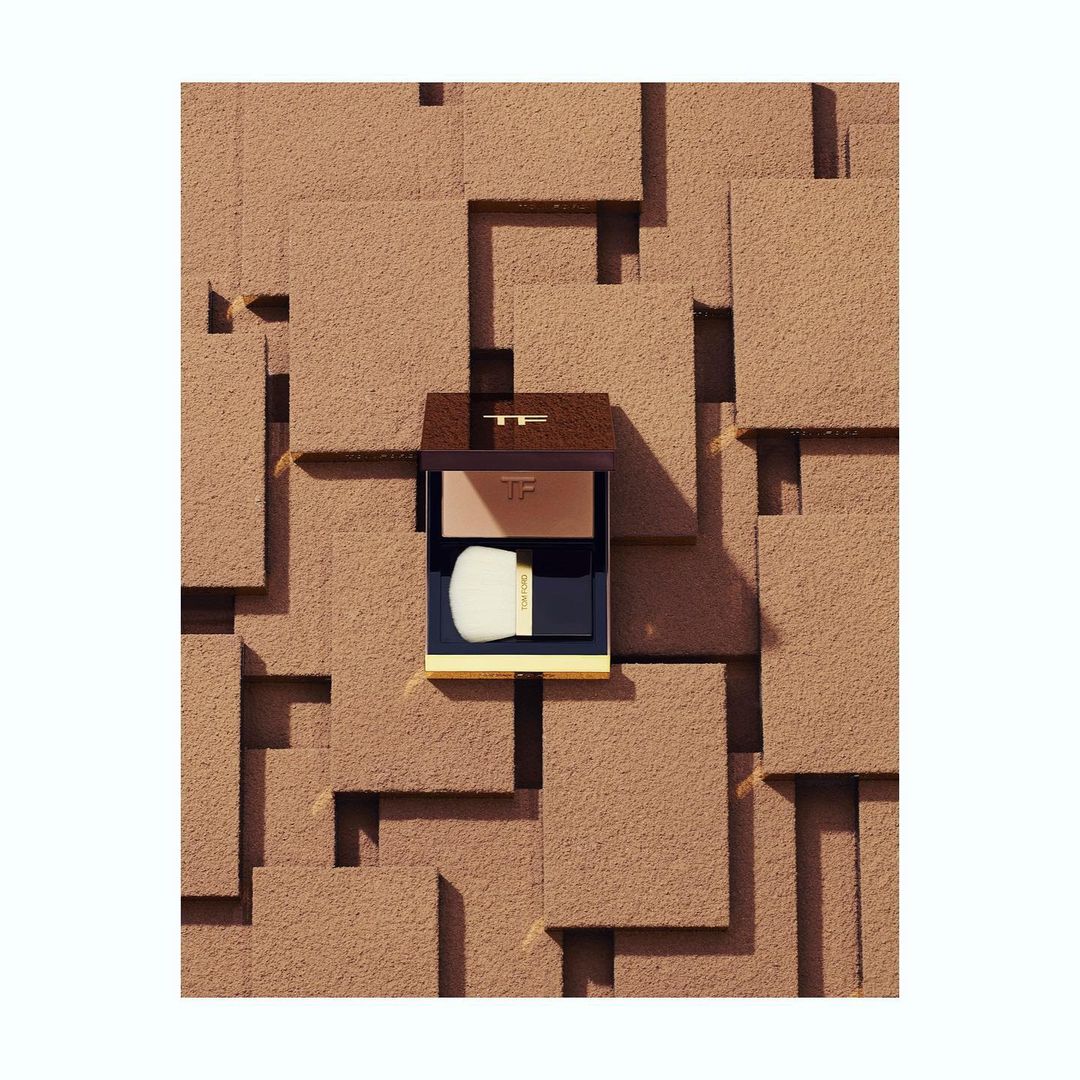 Tom Ford bronzer compact with application brush sits against a geometric textured background of brown, tan, and off-white squares.
