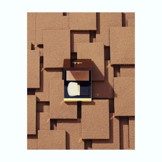 Tom Ford bronzer compact with application brush sits against a geometric textured background of brown, tan, and off-white squares.