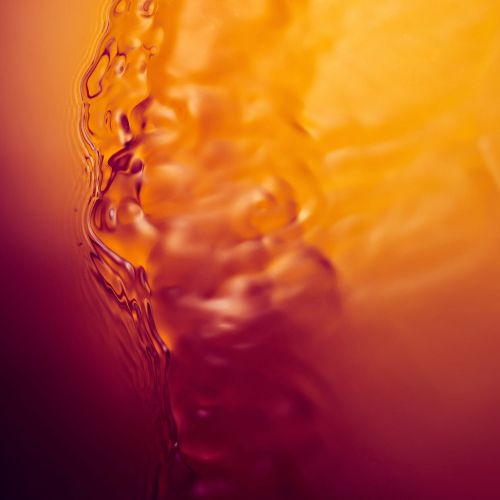 Abstract close-up of an orange liquid with rippling, translucent textures and a gradient of hues, creating a warm and dynamic visual.