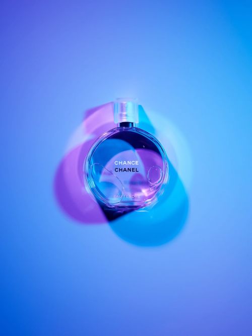 Glass perfume bottle of Chanel Chance on a gradient blue background, highlighted by pink and blue gels in a beauty still life.