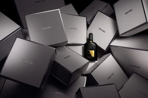A black perfume bottle surrounded by a chaotic stack of grey branded boxes under dramatic studio lighting.