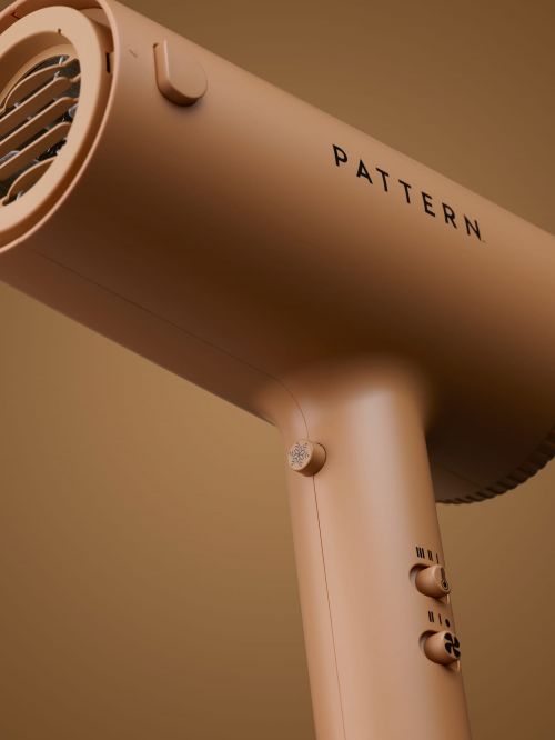 Close-up studio shot of a tan Pattern hair dryer, showcasing its design and features against a matching tan backdrop.