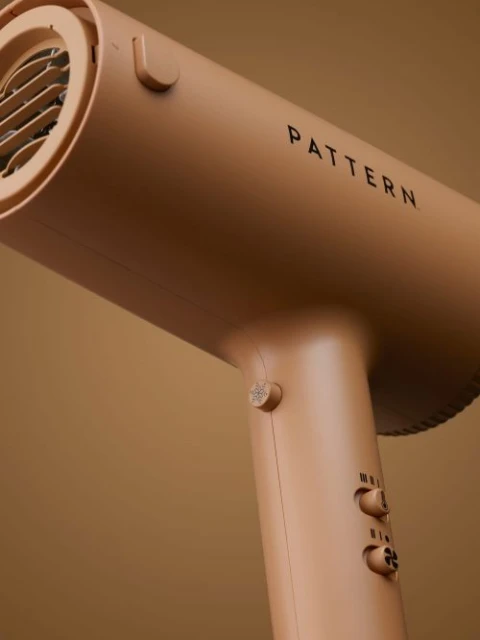 Close-up studio shot of a tan Pattern hair dryer, showcasing its design and features against a matching tan backdrop.