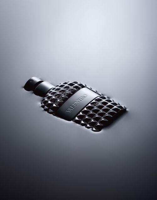 A bottle of Valentino perfume with a studded design, partially submerged in water, is prominently displayed in a sleek, monochromatic composition.