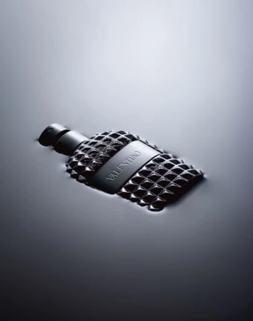 A bottle of Valentino perfume with a studded design, partially submerged in water, is prominently displayed in a sleek, monochromatic composition.