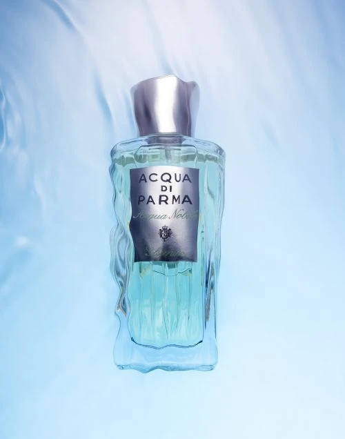 A bottle of Acqua di Parma Colonia Nobile perfume against a light blue background with a subtle water texture effect.