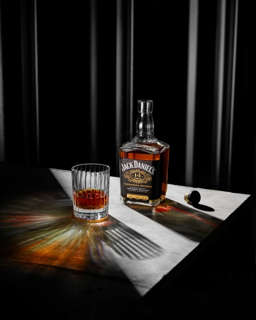 Still life shot of a bottle of Jack Daniel's whiskey with a glass, showcasing warm lighting and dark background with vertical linear details.