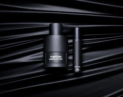 Two Tom Ford Ombre Leather perfume bottles, different sizes, side by side on rippled black surface. Elegant, minimalist, product shot.