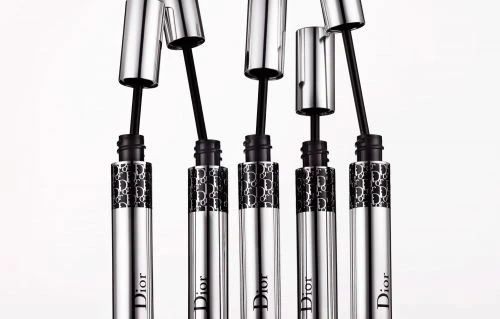 Five Dior mascara tubes with silver caps and black applicators on a white background, showcasing elegant and high-end beauty products.