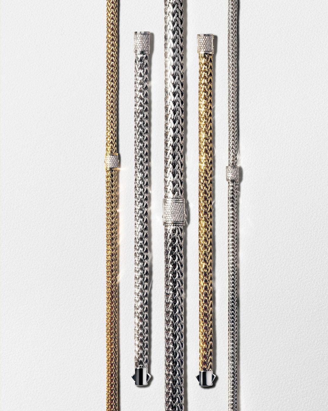 Elevated view of multiple gold and silver woven chain-link bracelets on white background. Jewelry fashion and accessories shot in studio.