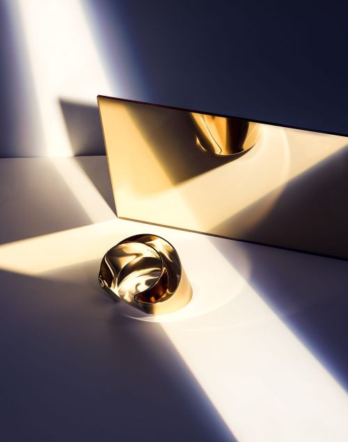 Abstract still life of a gold ring on a white surface with dramatic light and shadow patterns and a gold rectangular background.