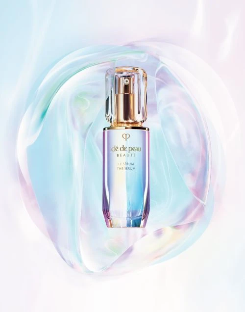 Cle de Peau Beaute Le Serum bottle showcased against an abstract, iridescent background. Beauty product shot for skincare promotion.