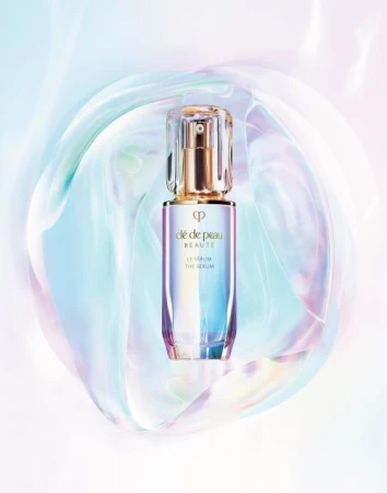 Cle de Peau Beaute Le Serum bottle showcased against an abstract, iridescent background. Beauty product shot for skincare promotion.