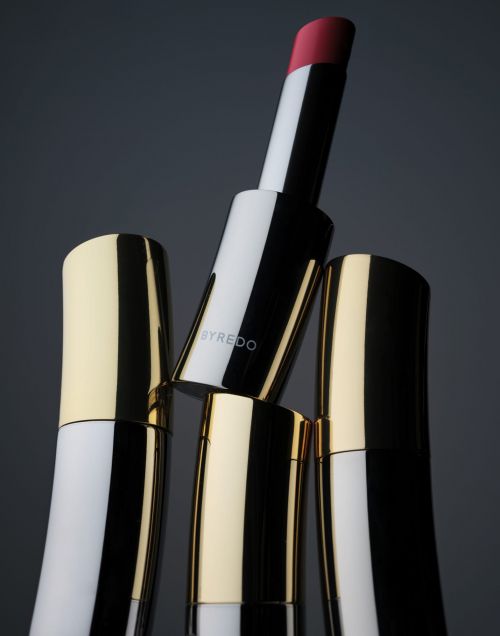 Product shot of Byredo lipstick tubes featuring gold, black, and white design with one extended tube revealing the pink lipstick.