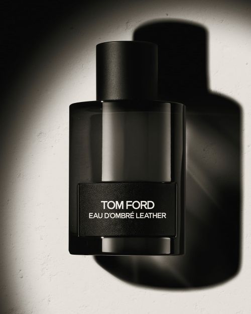 Tom Ford Eau dOmbre Leather perfume bottle in dark glass with a black cap against a light textured surface casting a strong shadow.