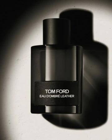 Tom Ford Eau dOmbre Leather perfume bottle in dark glass with a black cap against a light textured surface casting a strong shadow.